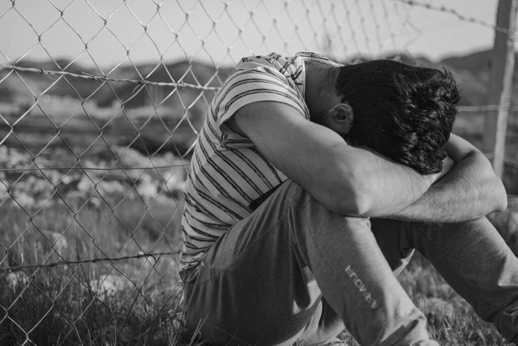 Man sitting on the ground, covering his head with his arms, in guilt and shame.