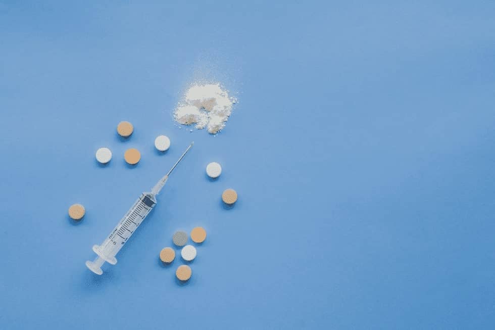 Syringe with pills and powder on a blue platform