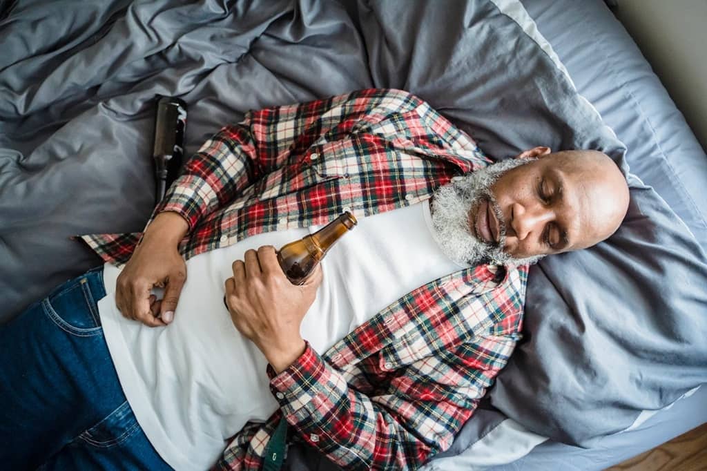 Alcohol addict lying on bed holding a bottle