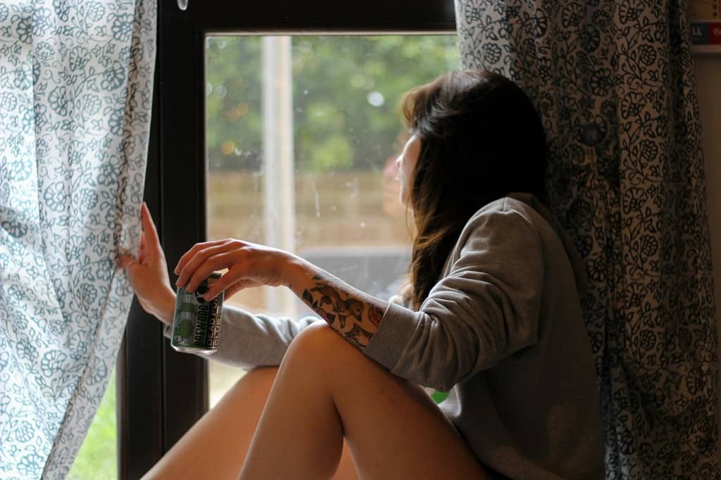 Woman with a tatoo on her hand looking out of the window holding an alcohol can