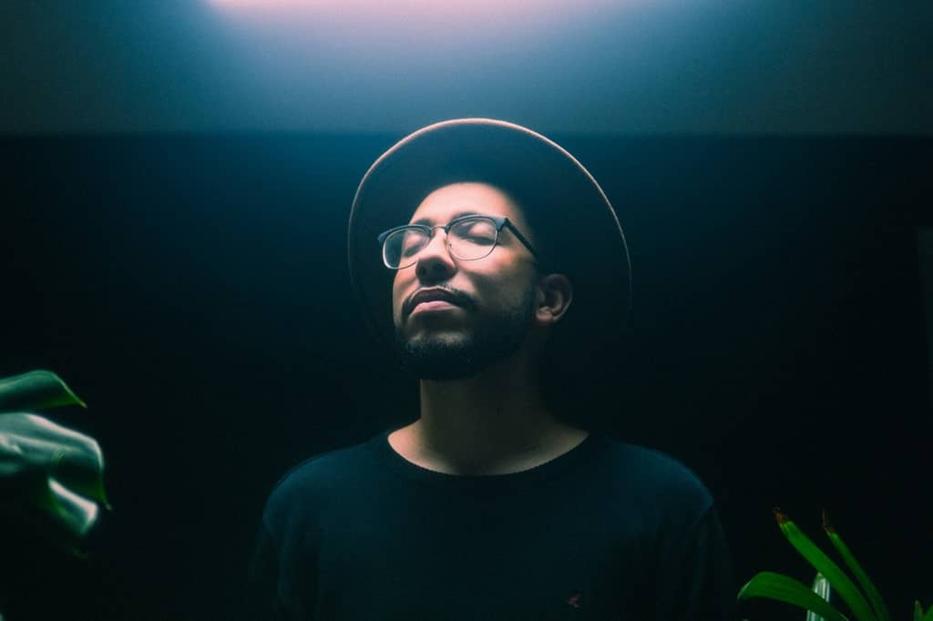 A man in a hat and glasses standing with closed eyes